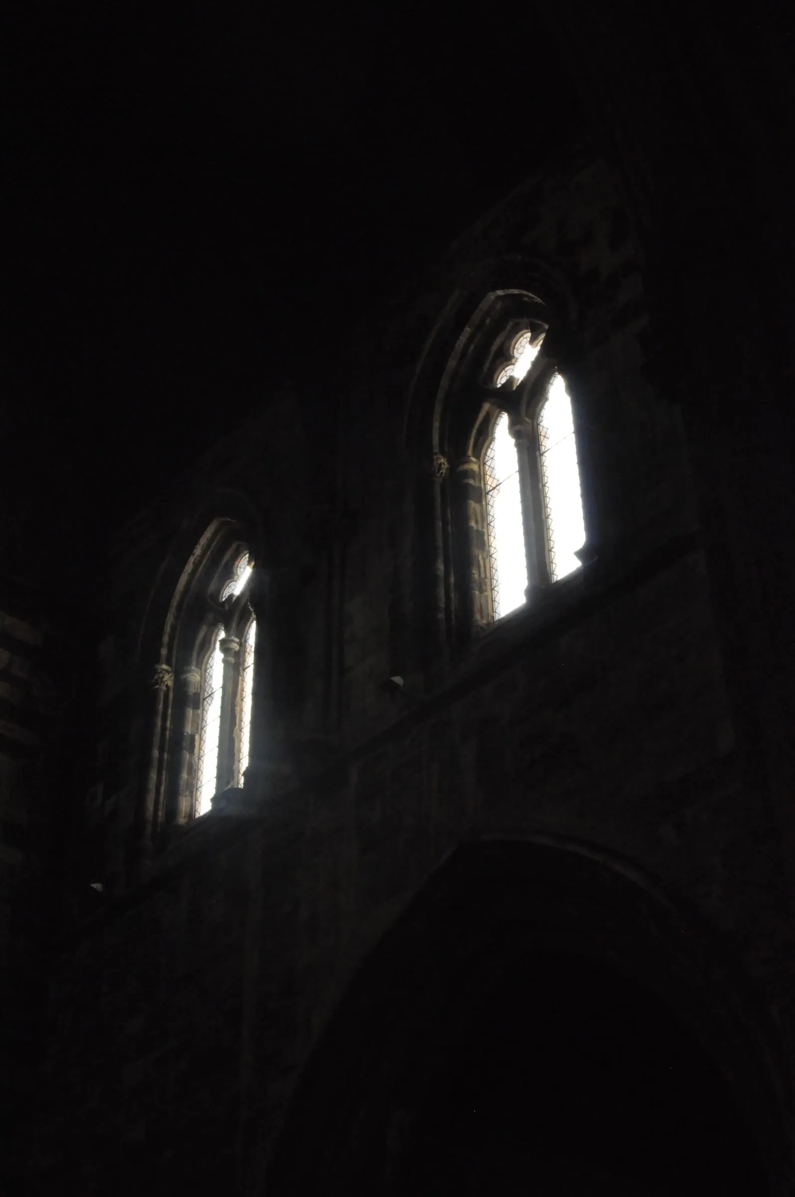 Two narrow arched windows glow in the darkness of a church interior.